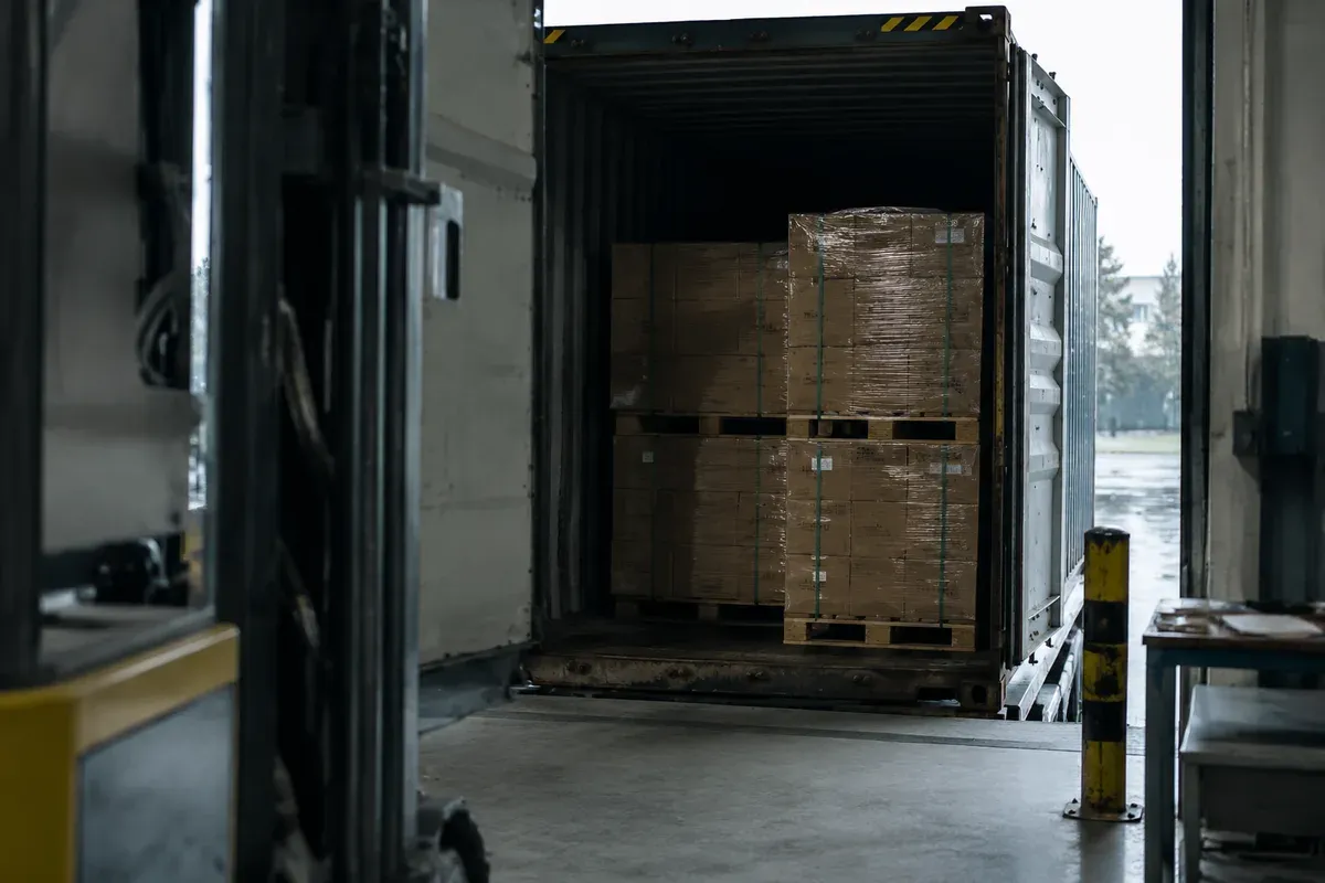 Palletised battery cartons at a loading bay beside a shipping container
